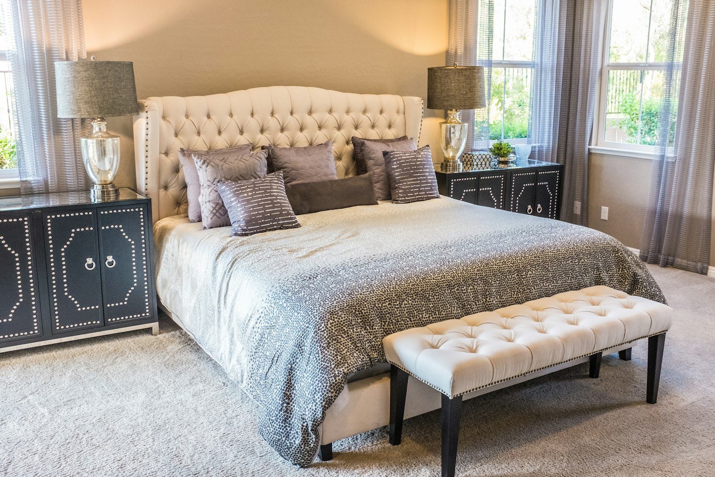 Bedroom with a cream buttoned headboard, grey patterned bedding, and a cream bench at the foot of the bed