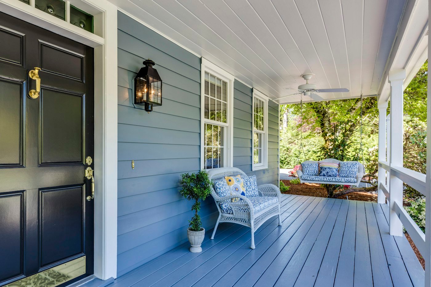 Pale blue porch with a black front door, a white wicker bench, and a hanging swing